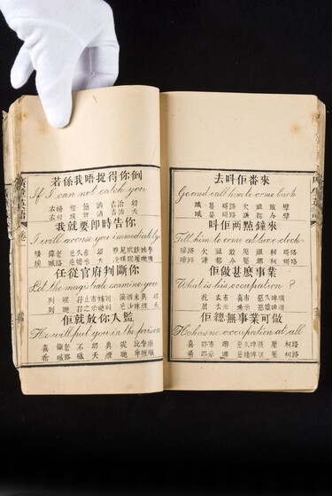 Double page book with Cantonese characters and English translations, being held by a hand with a white glove on.