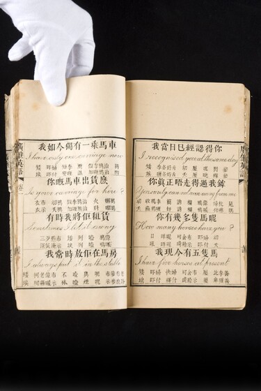 Double page book with Cantonese characters and English translations, being held by a hand with a white glove on.