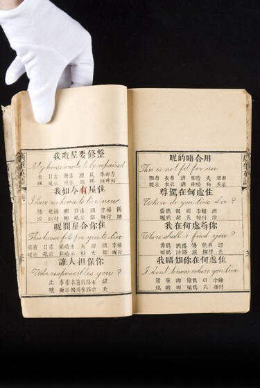 Double page book with Cantonese characters and English translations, being held by a hand with a white glove on.