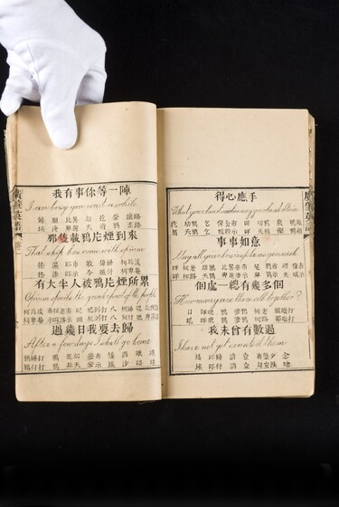 Double page book with Cantonese characters and English translations, being held by a hand with a white glove on.