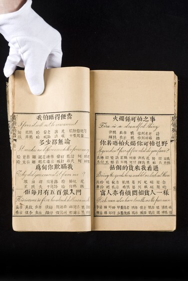 Double page book with Cantonese characters and English translations, being held by a hand with a white glove on.
