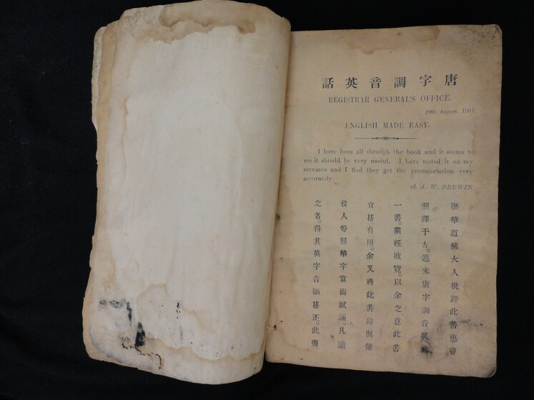 Double page book, the left hand side blank and slightly ripped and damaged, the right hand side featuring Cantonese characters and English wording.