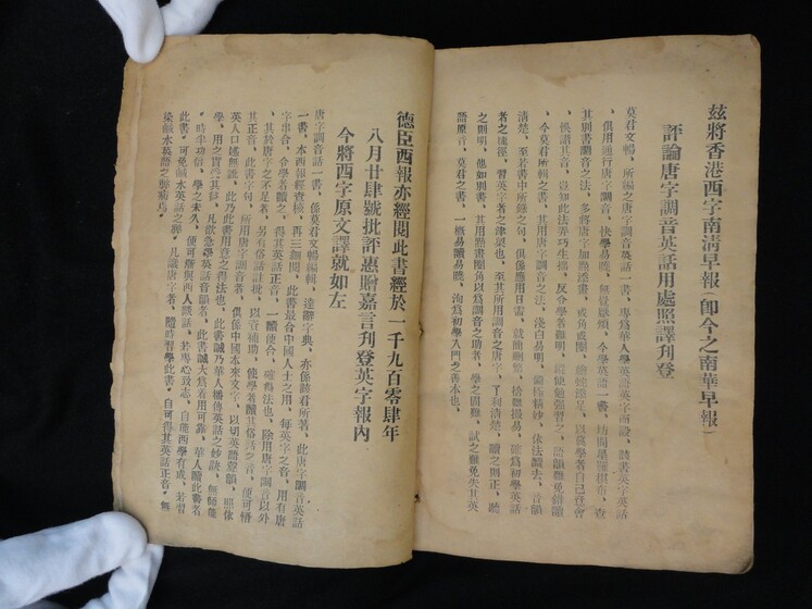 Double page book with Cantonese characters on both sides, being held by hands in white gloves.