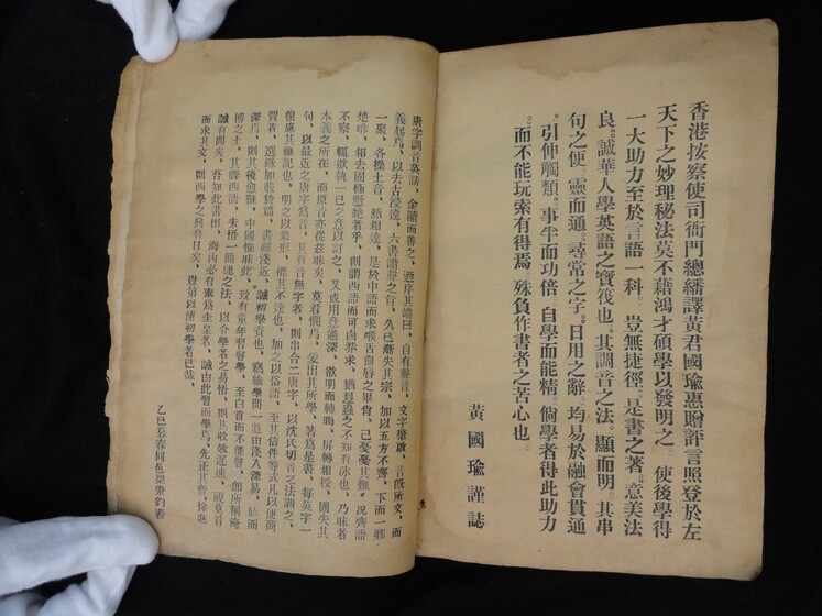 Double page book with Cantonese characters on both sides, being held by hands in white gloves.