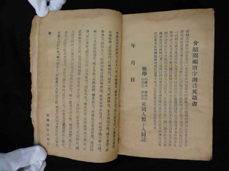 Double page book with Cantonese characters on both sides, being held by hands in white gloves.