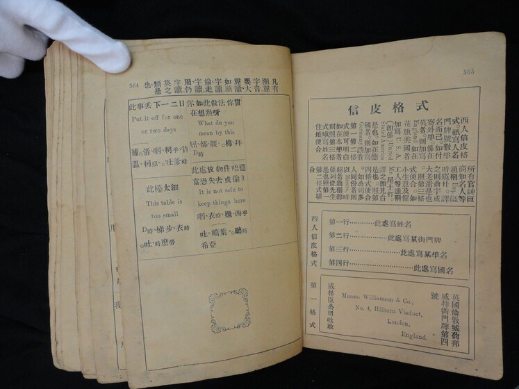 Double page book with Cantonese characters and English translations, being held by a hand with a white glove on.
