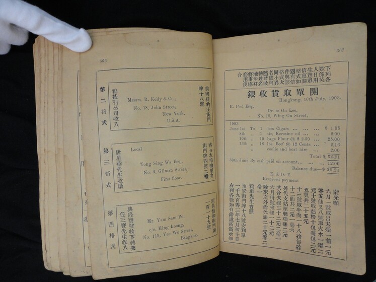 Double page book with Cantonese characters and English translations, being held by a hand with a white glove on.