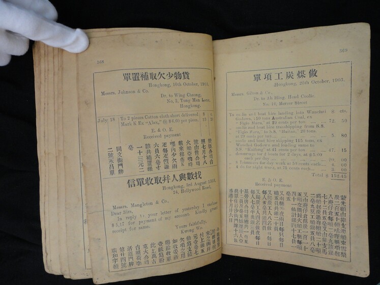 Double page book with Cantonese characters and English translations, being held by a hand with a white glove on.