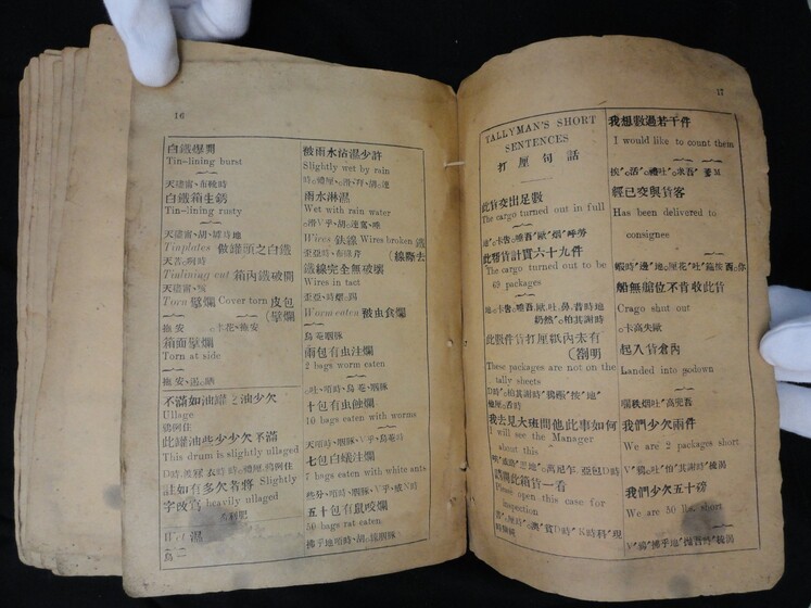 Double page book with Cantonese characters and English translations, being held by a hand with a white glove on.