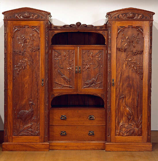 A decorative dark brown wooden wardrobe, with decorative paneling on all four doors, including birds, foliage and possums.