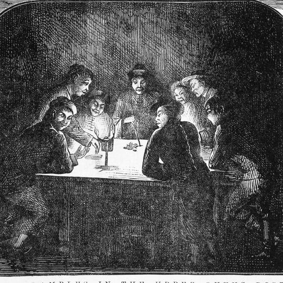 Black and white drawing of a group of Chinese men leaning over a card table, a candle lighting the room to show the men's faces. 