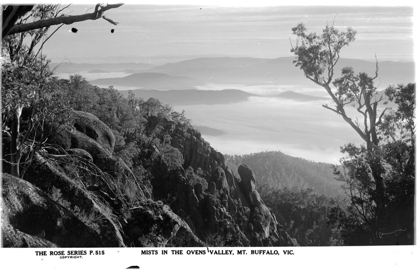 Black and white landscape photograph, taken from the top of a mountain looking down into the valley, mist covering the tree tops.