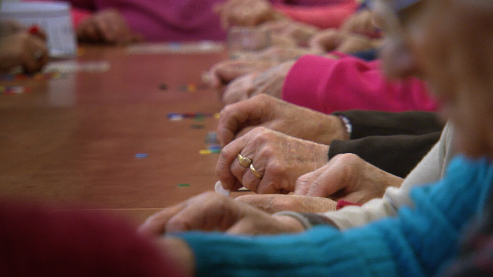 A somewhat out of focus photograph of a group of ladies arms, each in a different coloured long sleeve top, their arms resting on a wooden table.