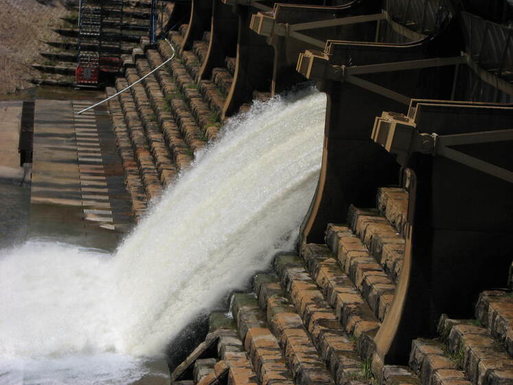 A weir made up of cement staggered steps with a large amount of water gushing over the edge.