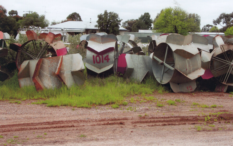A large pile of metal water wheels sit in a pile on the side of a dirt track, all positioned at different angles.