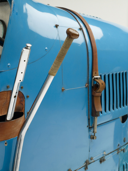 A close up view of the side of the car, including the gear stick and the leather straps that hold the bonnet in place.