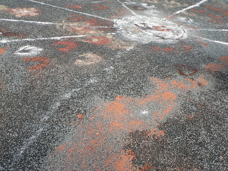 A close up view of the sand artworks on the black bitumen, made up of orange colours, white lines and hand prints.