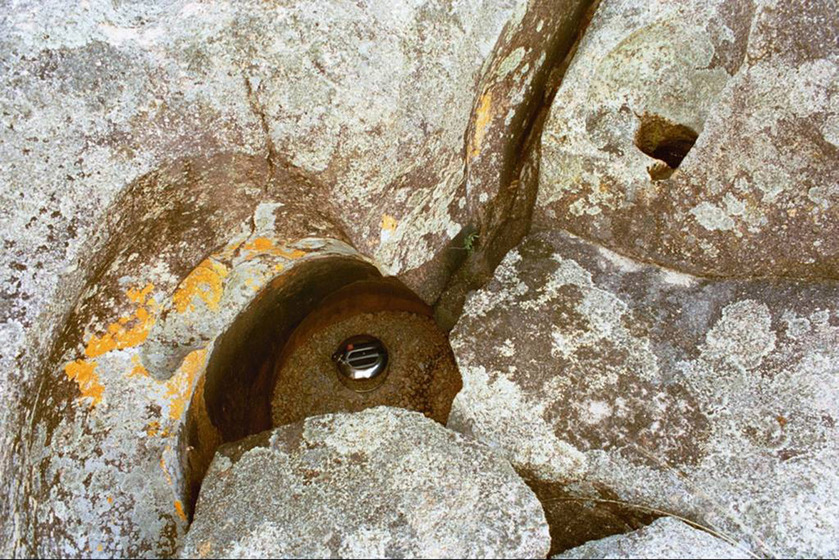 A photograph of a metal kettle floating in a river, large rocks positioned around the edge of the water.