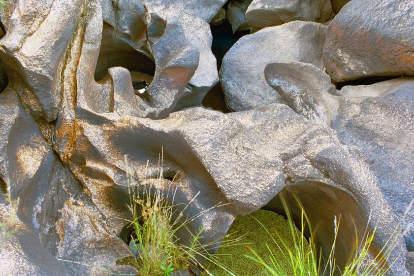 A photograph of a metal kettle positioned on large river rocks, shaped and softened by the flow of the water over many years
