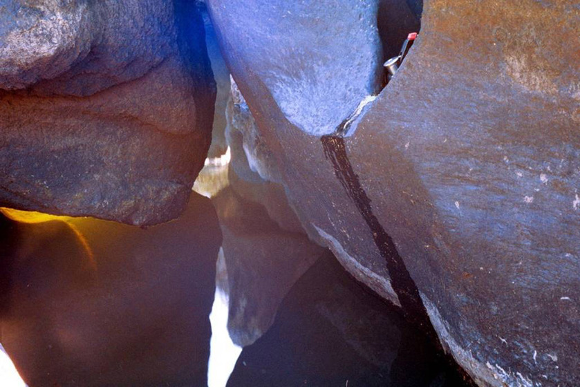 A photograph of a puddle of water positioned in amongst large river rocks, the reflections of the rocks bouncing up off the water.