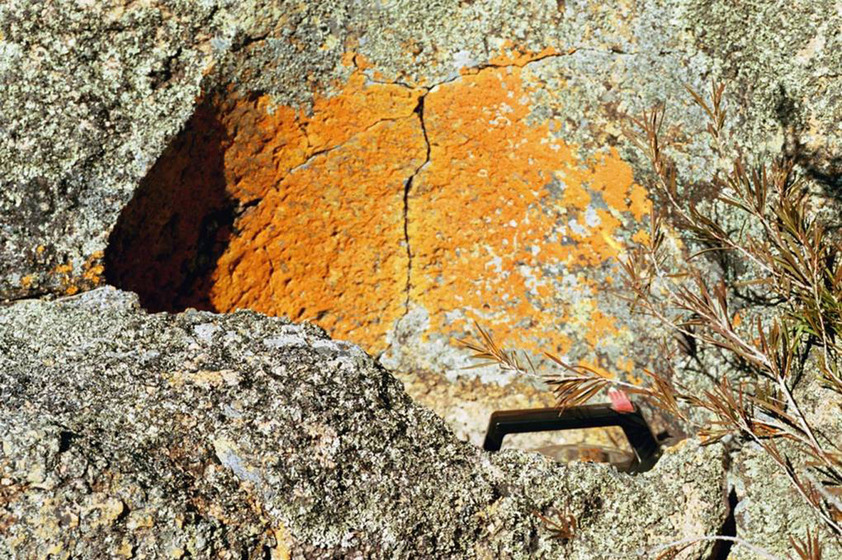 A photograph of river stone, the bright yellow markings indicating where water once ran. The handle of the metal kettle can be seen just above the rock edge.