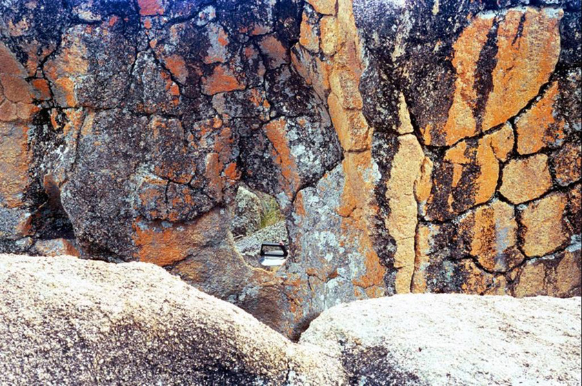 A photograph of river stone, the bright yellow markings indicating where water once ran. The handle of the metal kettle can be seen just above the rock edge.