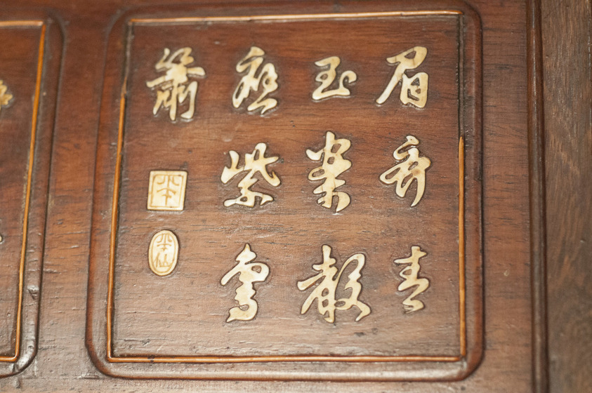 A wooden panel is engraved with gold chinese characters. They are placed across three rows, inside a curved square shape.