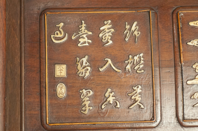 A wooden panel is engraved with gold chinese characters. They are placed across three rows, inside a curved square shape.