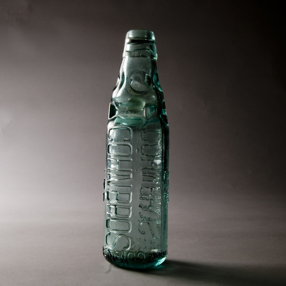 Blue glass bottle, slightly transparent, with ridge marks and raised writing on the side of the bottle.