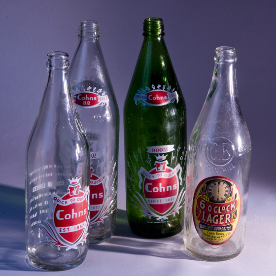 Four glass bottles of differing heights and sizes with different labels, all sporting the 'Cohns' brand.