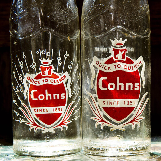 Two glass bottles sitting side by side, both with red and white labels of different sizes.