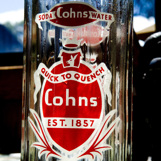 A glass bottle with a red and white label on the front. The bottle has ridging running vertically down the sides of the bottle.