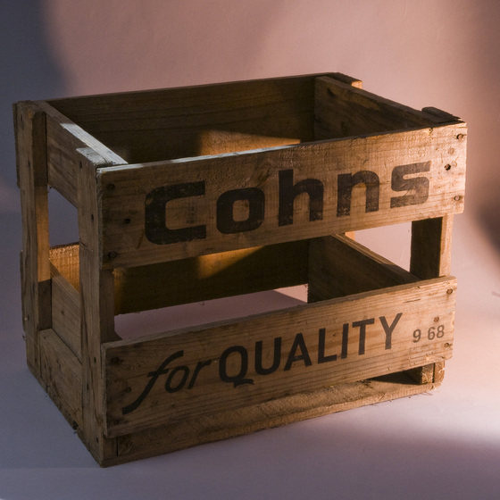 Wooden crate with slats going both horizontal and vertical. Printed on the side in black text is 'Cohns for Quality'.