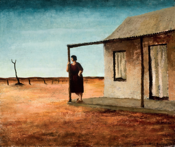 Woman in dark dress standing leaning against the post of a shack in an arid flat orange landscape with a dead tree in the distance.