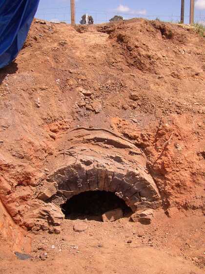 A partially submerged brick structure, in the shape of a semi circle. It is submerged in the red soil of the hill side.