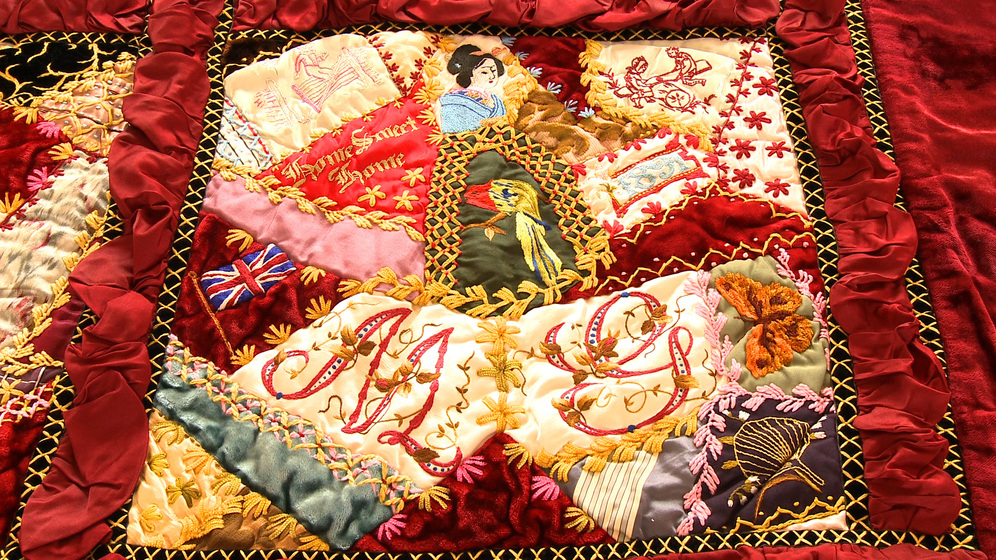 A panel on a patchwork quilt, made up of various pieces of different coloured fabric and embroidered images and stitches over the top.