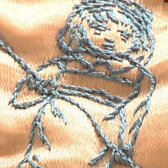 A hand stitched figure of a girl, in light blue, holding on to a pole of some kind in her hands.