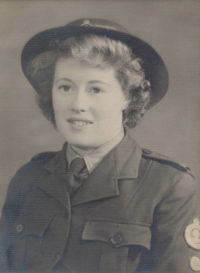 Studio torso portrait of a young woman wearing a military uniform jacket and hat.
