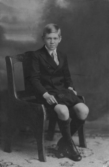 A young boy wearing a suit and shorts, seated in a studio portrait.