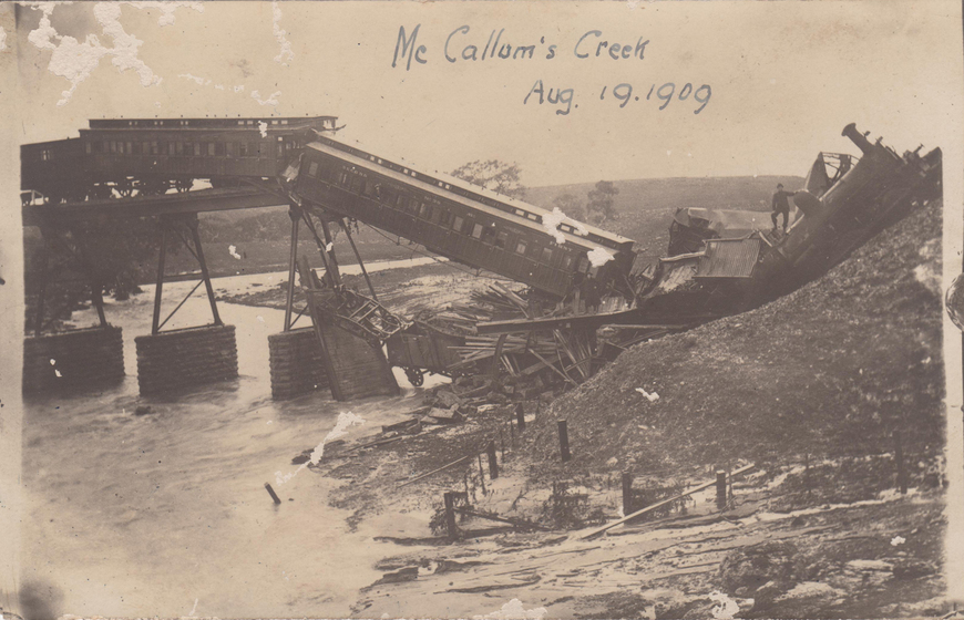 Train carriages that have crashed off a collapsed bridge crossing a river. Handwritten text on the image above reads 'McCallum's Creek Aug 19.1909.