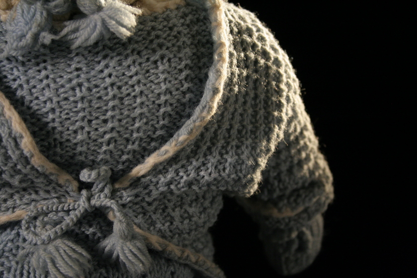 Close up detail of a doll's torso, wearing a light blue woollen crochet jacket.