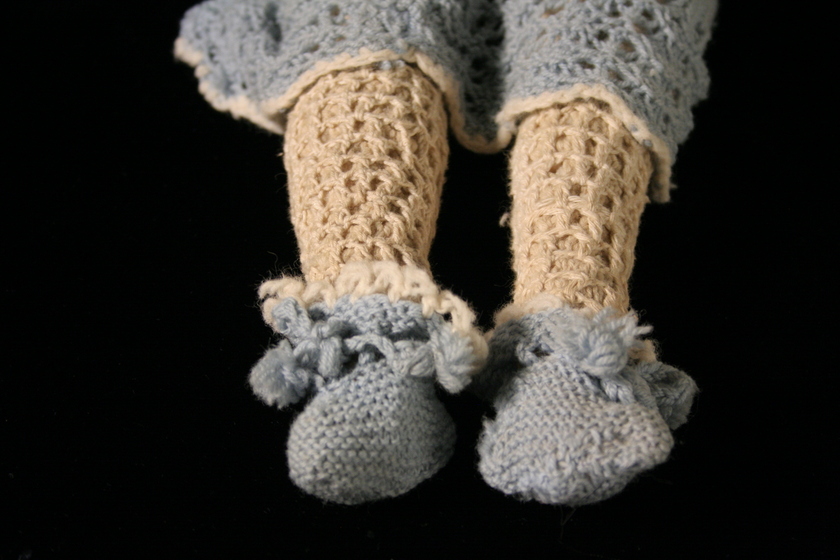 Close up detail of a woollen doll's legs and feet, showing light blue woollen croquet dress hem and shoes.