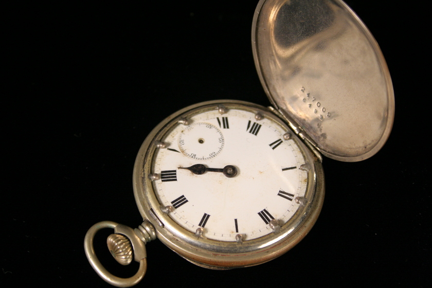 Close up of an open silver fob watch with roman numerals on the face.