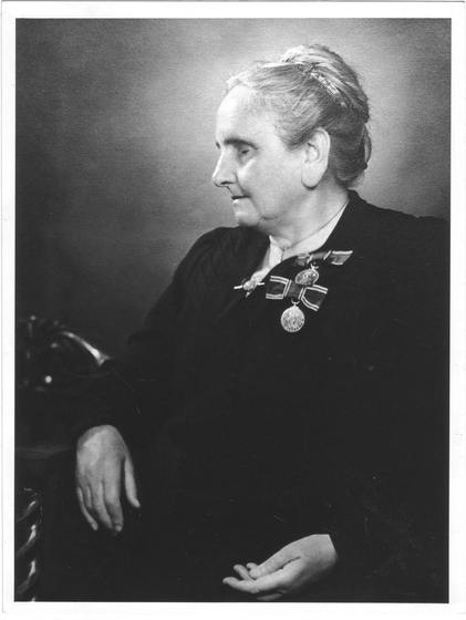 Studio torso portrait of an elderly woman wearing black. Two medallions feature on her lapel,