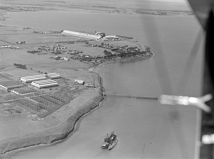 Arial view of a large body of water meeting land with industrial buildings. A ship can be seen at the bottom of the image.