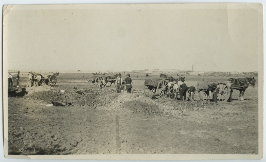 Dirt ground and mounds, with men working alongside horses pulling carts.