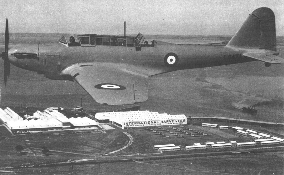 Arial view of a one-man plan taken alongside. Plan has a propeller and target circles on the wing and side. Seen below on the ground is a large industrial set of buildings with the words on the side reading 'International Harvester'.