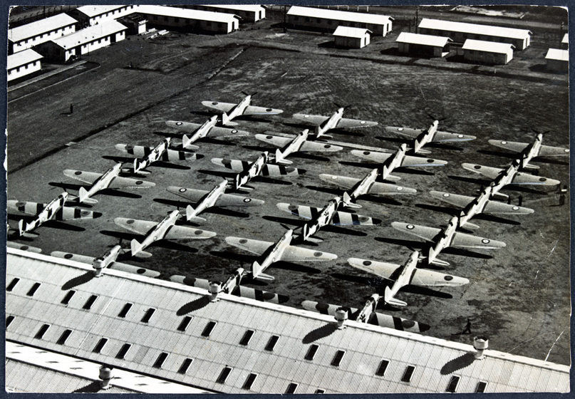 Aerial view of rows of one-person plans, four rows of six planes, surrounded by buildings on three sides.