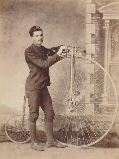 Man standing beside a penny farthing bicyle.