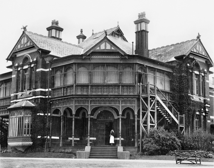 Exterior of an ornate two story building. A woman dressed in a nurse outfit stands on the entry steps.